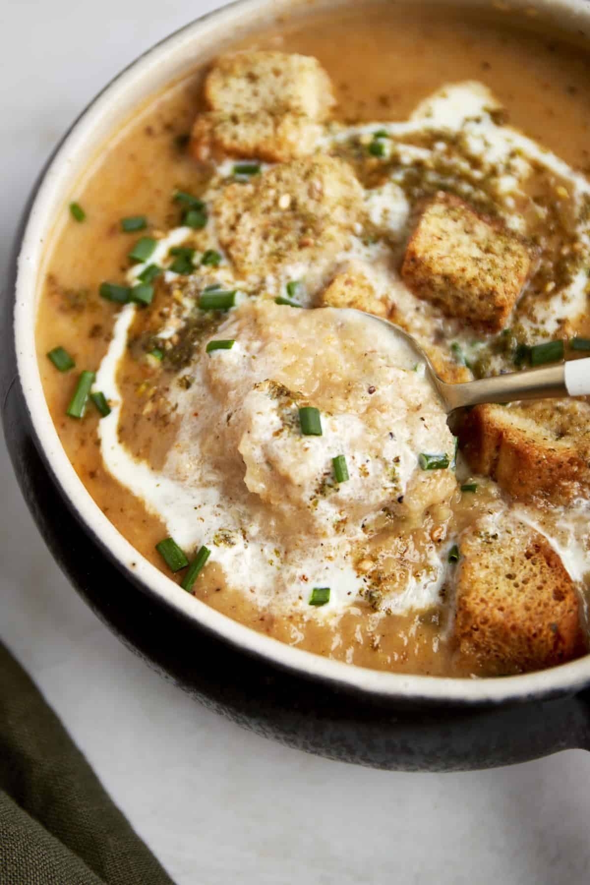 A spoon lifting a bite of roasted cauliflower soup from a bowl.