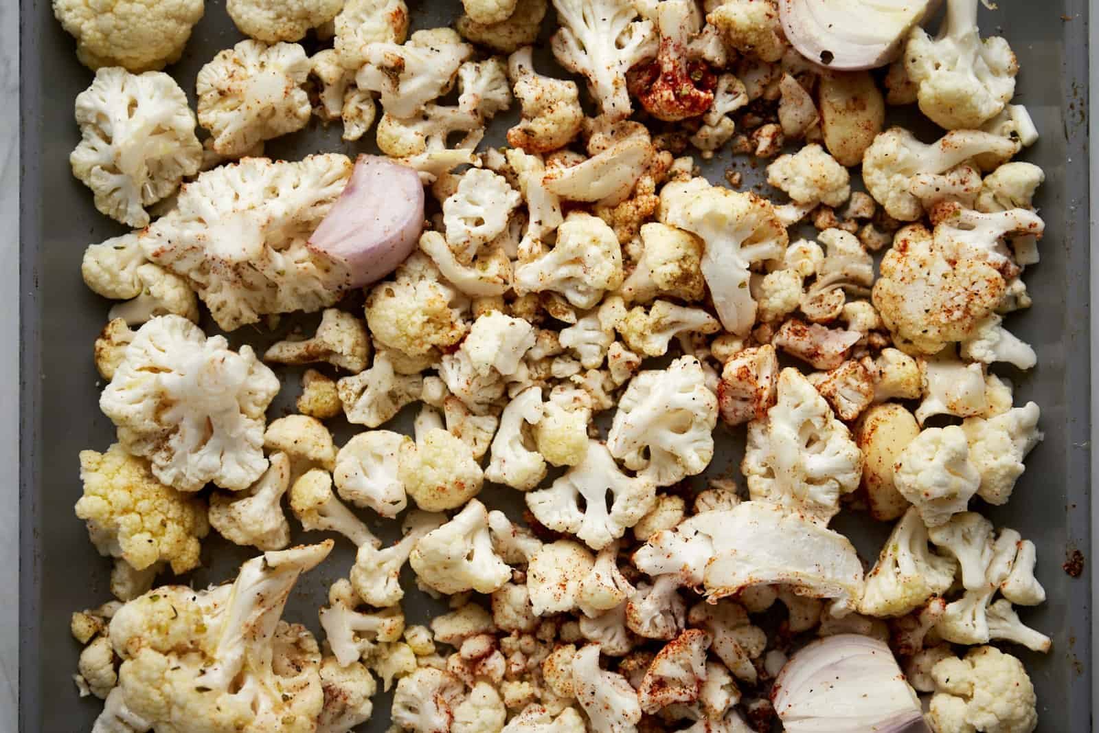 Seasoned cauliflower, shallots, and onions on a baking sheet.