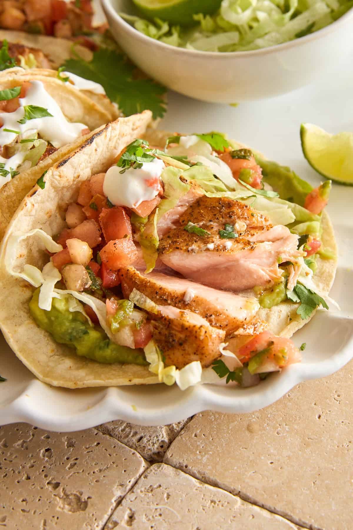 A salmon taco with lettuce, guacamole, and pico de gallo.