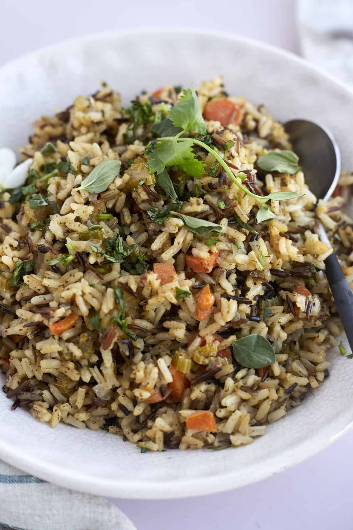 a bowl of seasoned rice topped with fresh herbs with a spoon on the side