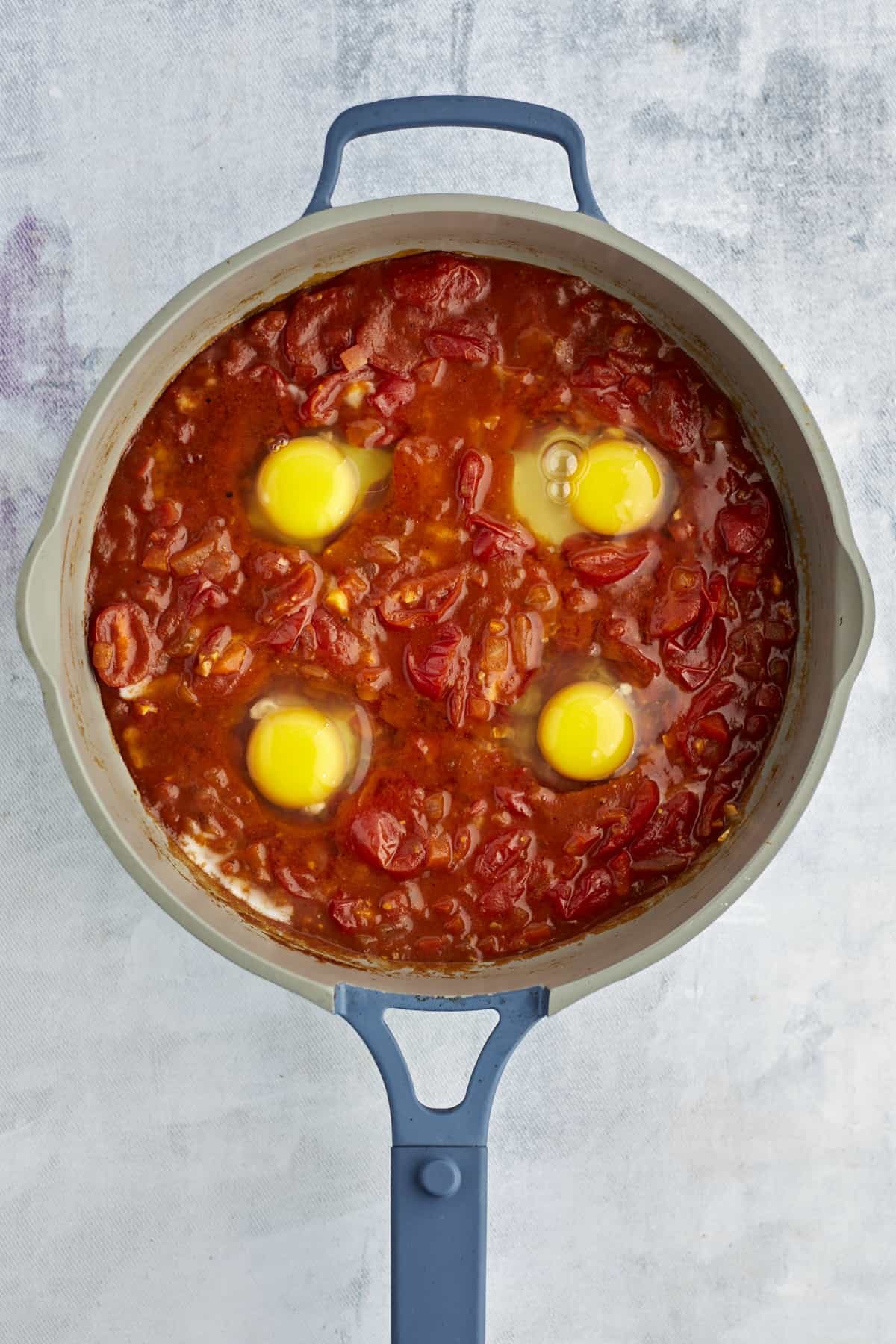 four eggs cracked into shakshuka sauce in a large pot