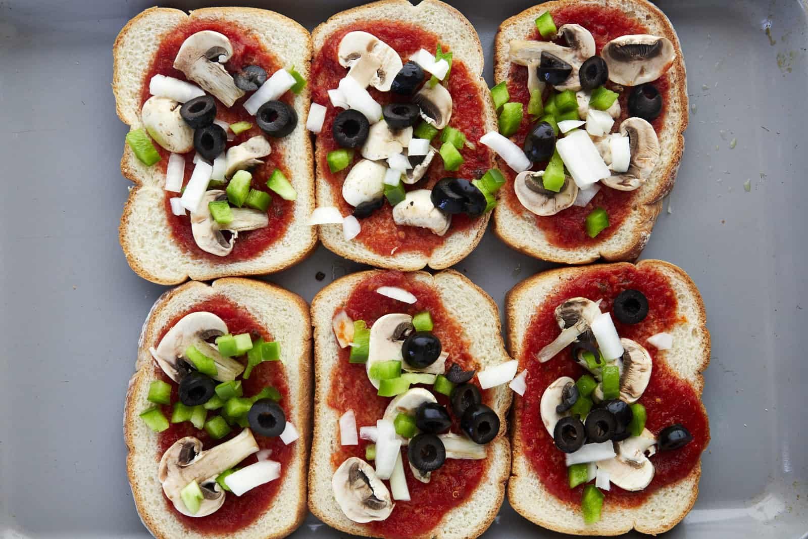 Marinara spread over pieces of bread topped with mushrooms, onions, and peppers.