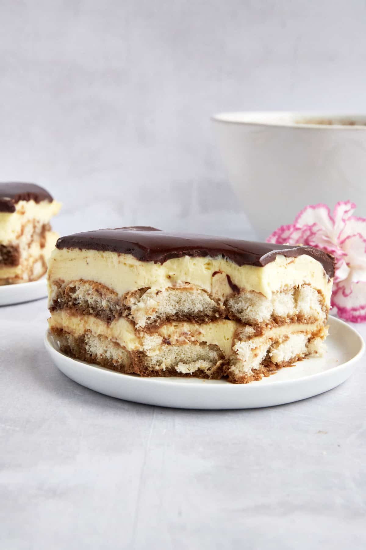 Tiramisu eclair cake on a plate with a bite missing from the corner.