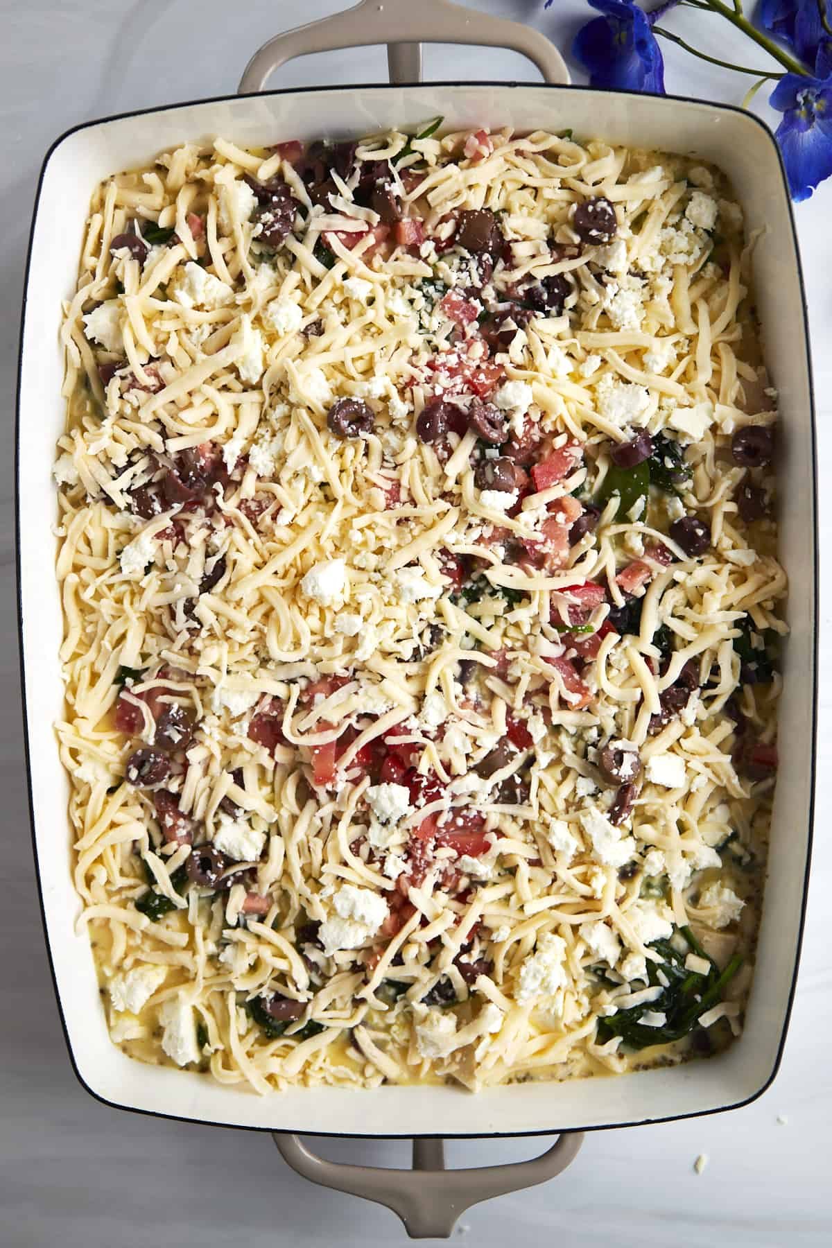 Feta and mozzarella cheese over an egg and veggie mixture with pita bread in a casserole dish.