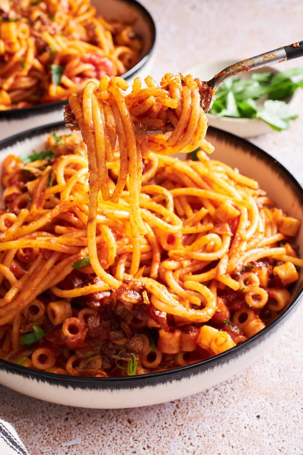 A fork lifting a bite of koshary-inspired Egyptian pasta from a bowl.