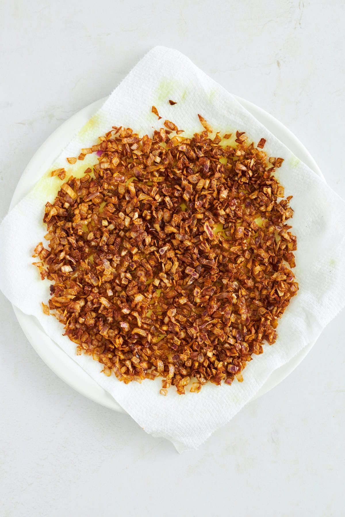 Fried onions draining on a paper towel-lined plate.