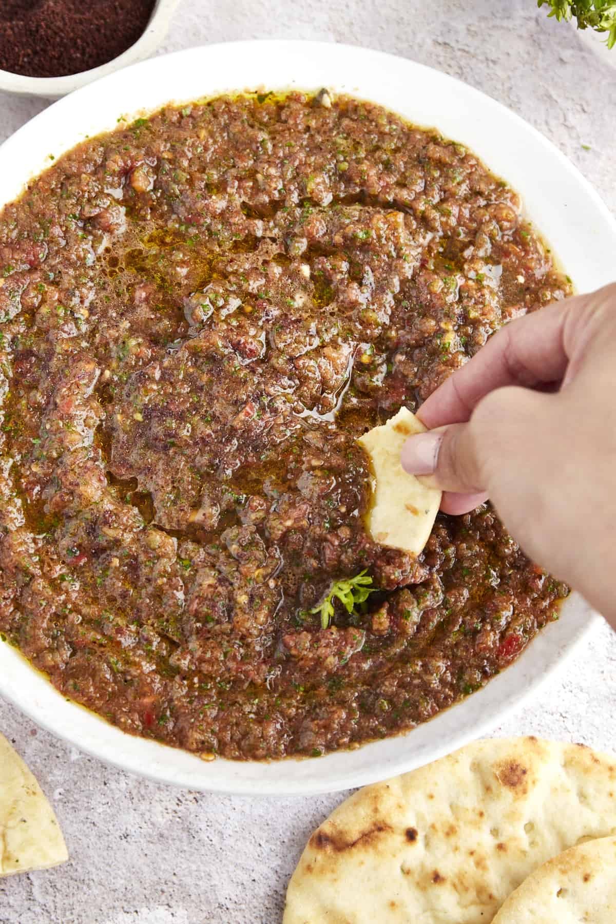 A hand dipping pita bread into a bowl of ezme.