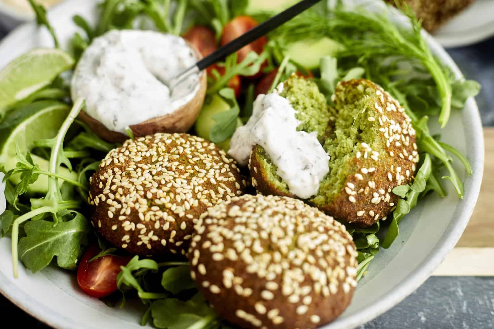 a salad with a small bowl of tzatziki and two whole falafel balls and a third split in half