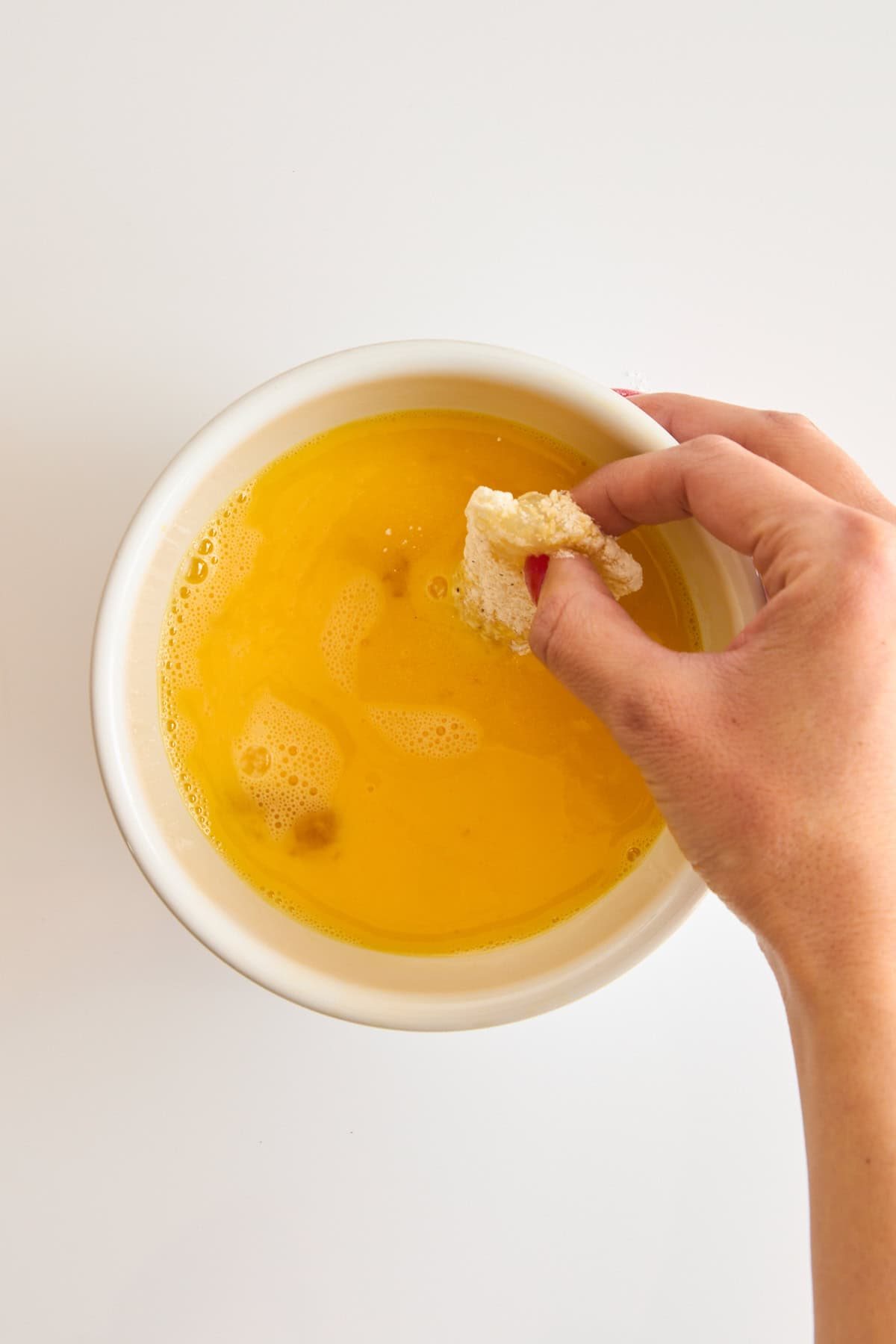 A flour coated cod piece being dipped into a bowl of whisked egg.
