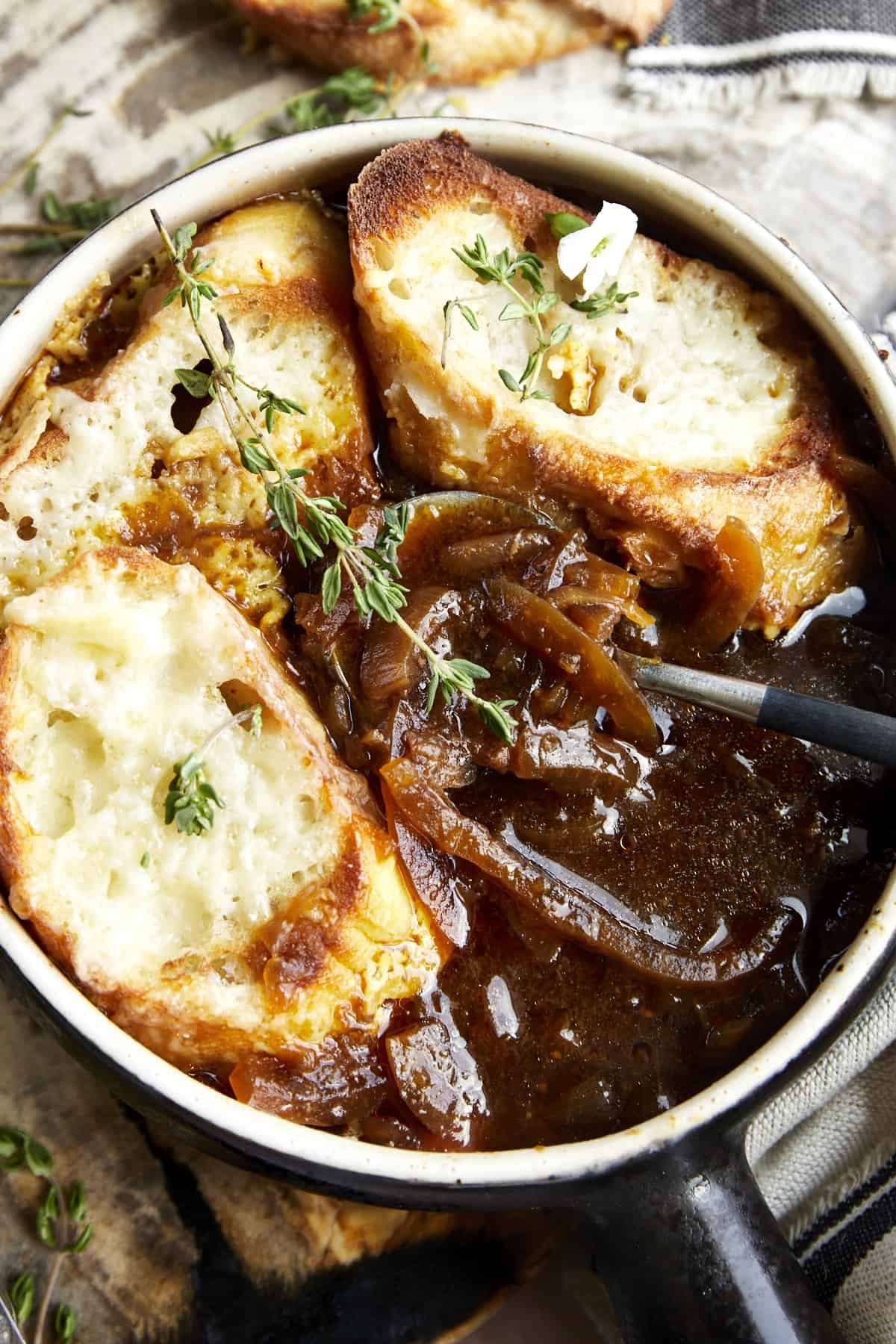 A spoon dipping into a bowl of easy French onion soup with a bread and cheese topping.