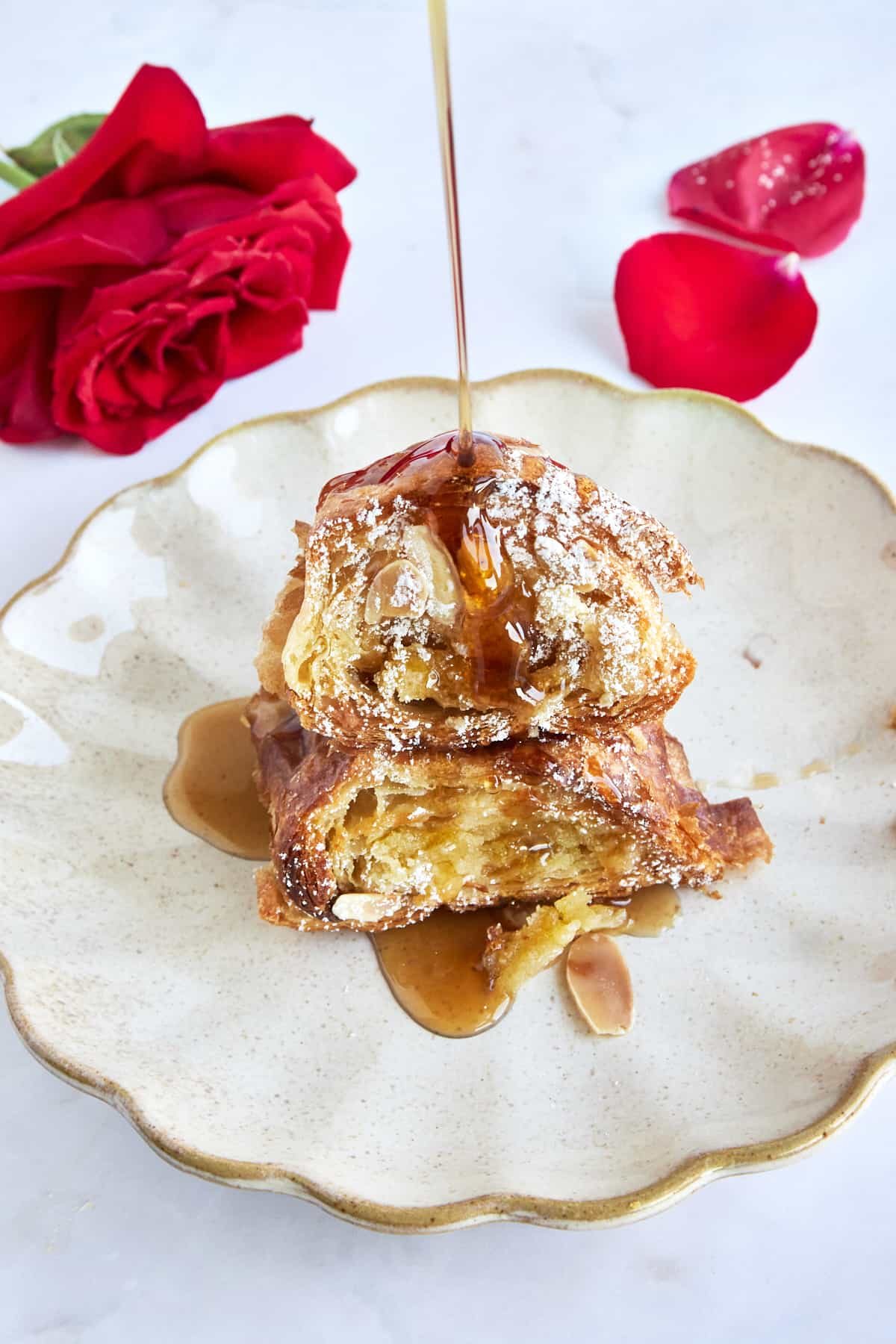 Syrup being drizzled over croissant French toast with almonds on a plate.