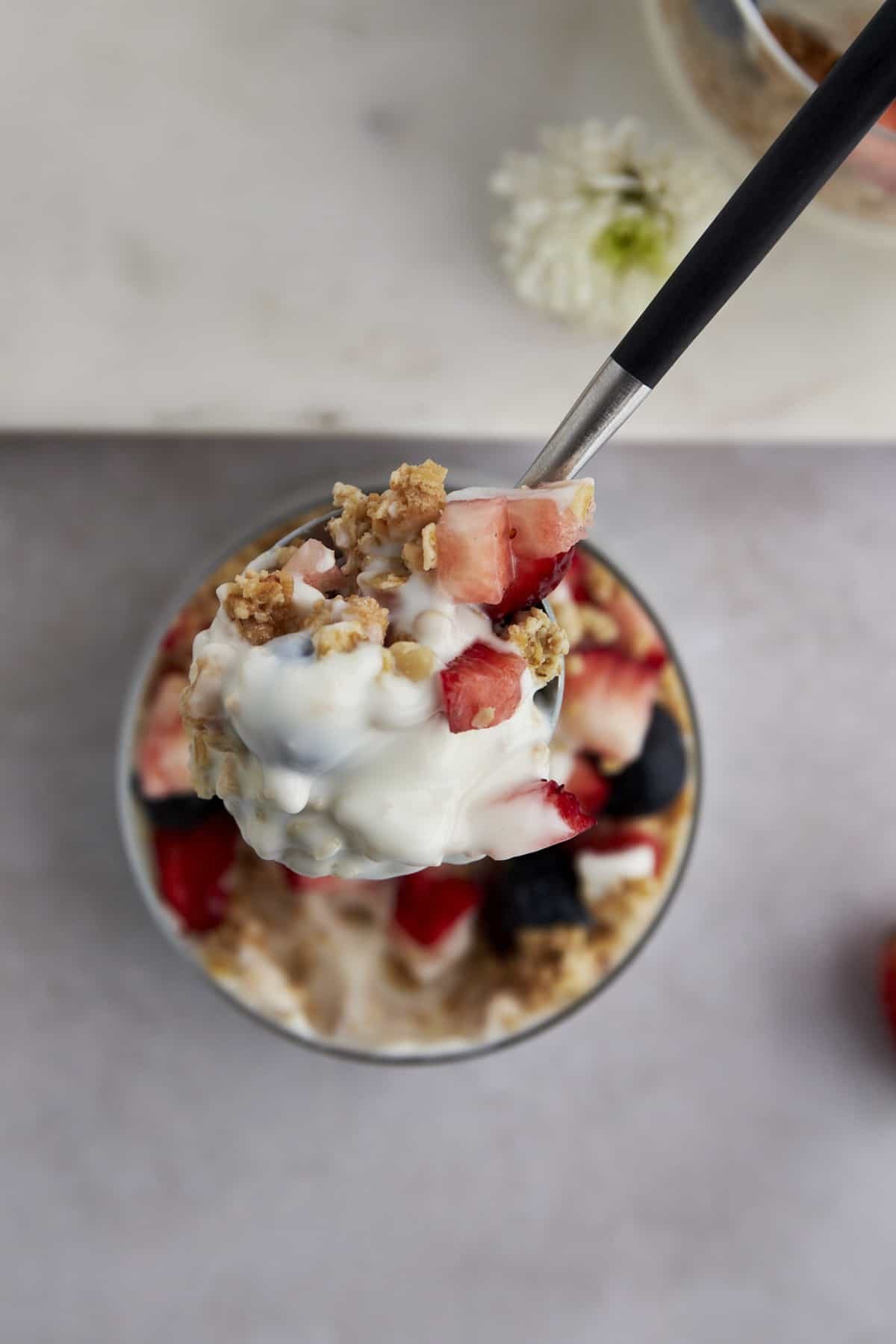 A spoonful of a yogurt parfait with granola, blueberries, and strawberries.