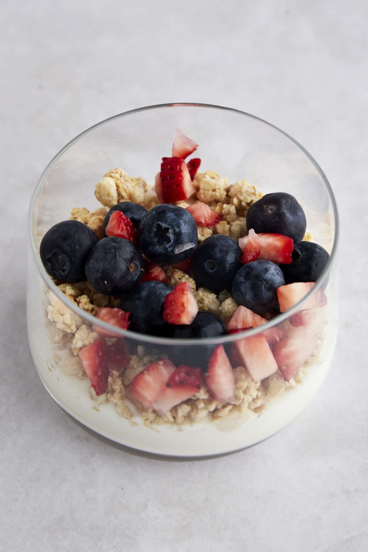 A glass jar with yogurt, granola, chopped strawberries, and blueberries.