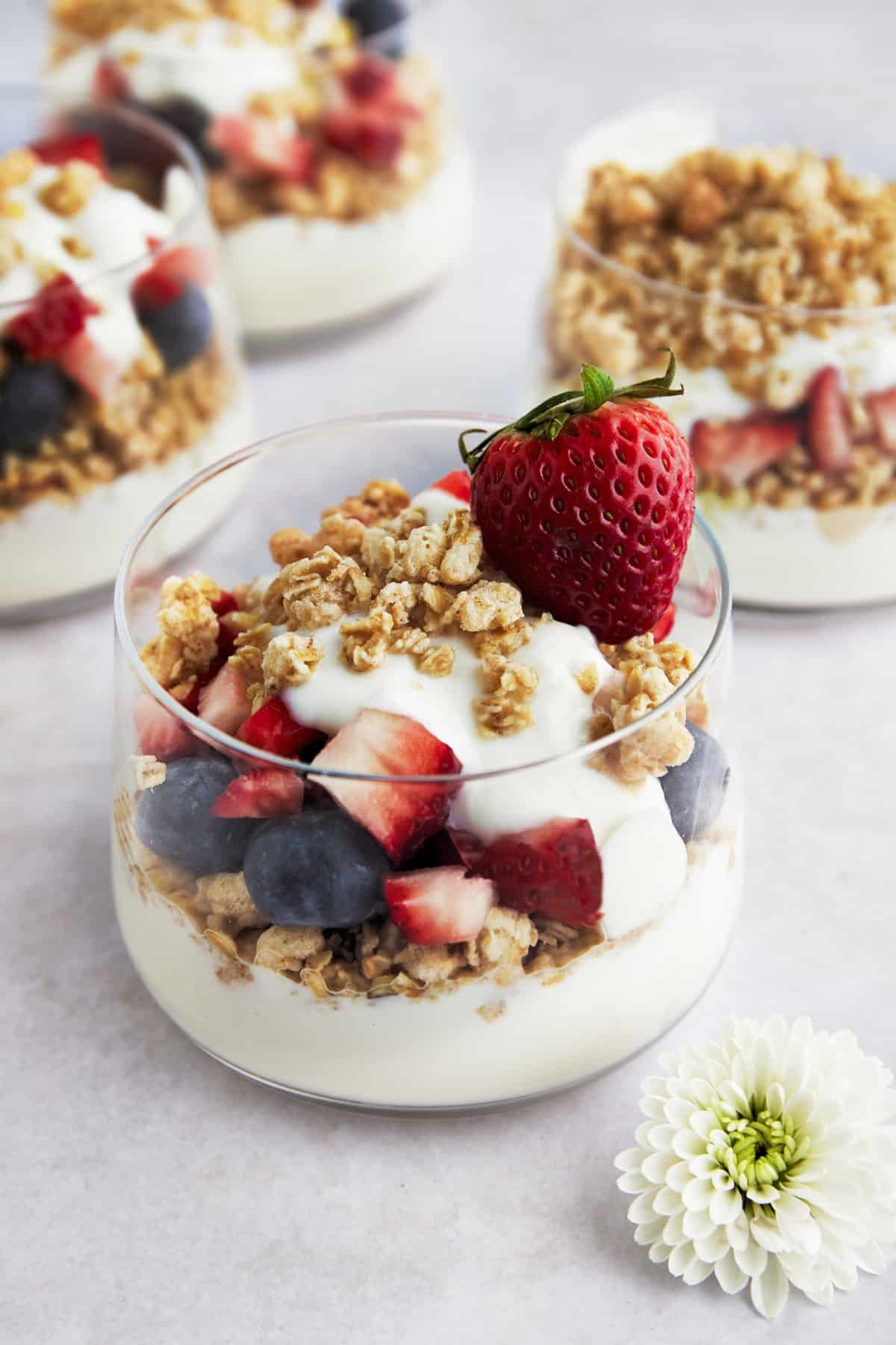 A fruit an yogurt parfait with granola, blueberries, strawberries, and honey.