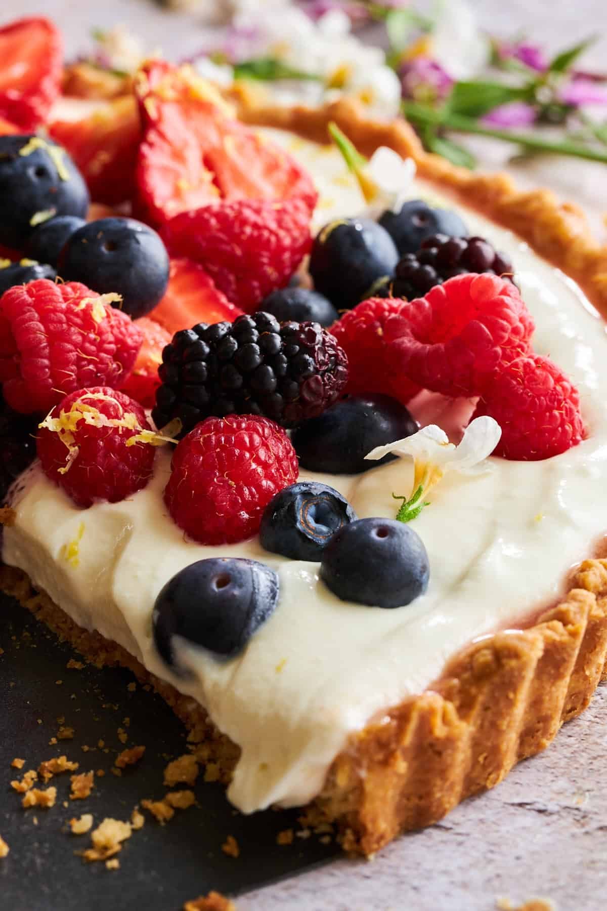 Side view of a cheesecake fruit tart topped with fresh raspberries, blackberries, and blueberries.