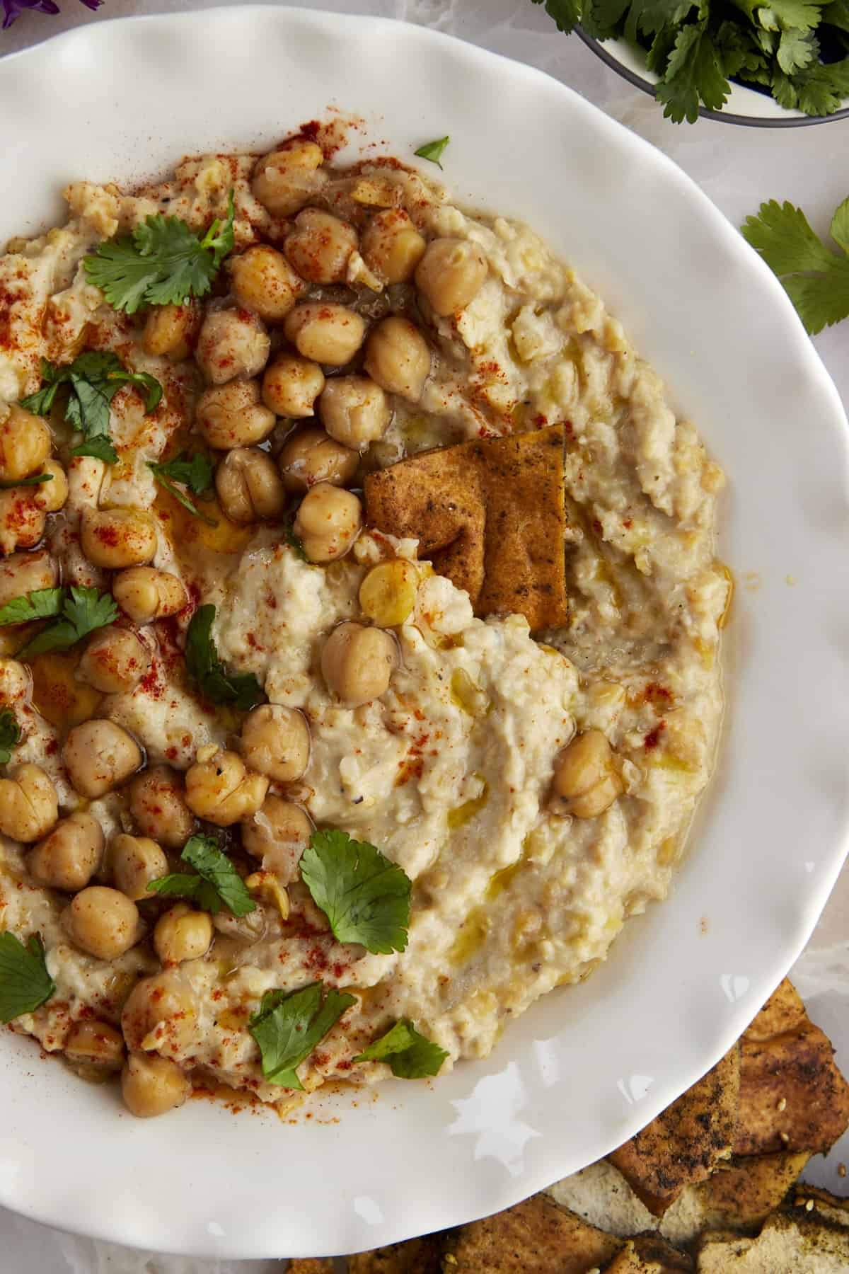 a pita chip dipping into a bowl of chunky garlic hummus (masabaha)