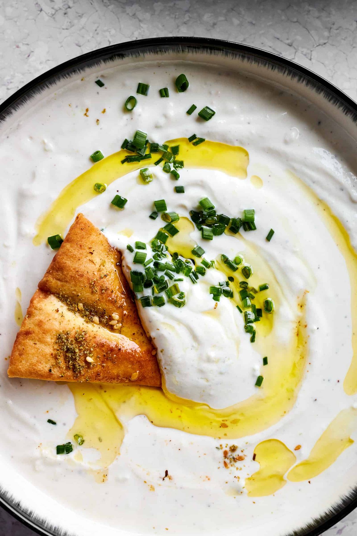 A pita chip dipped into a bowl of garlic yogurt sauce.