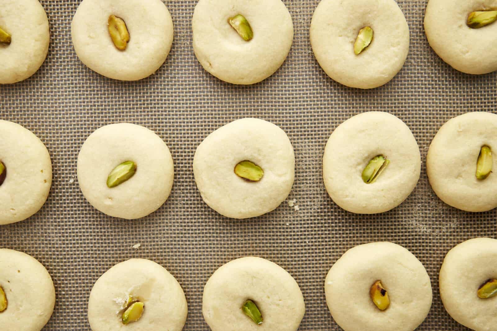 Baked graybeh cookies topped with pistachio halves on a baking sheet.