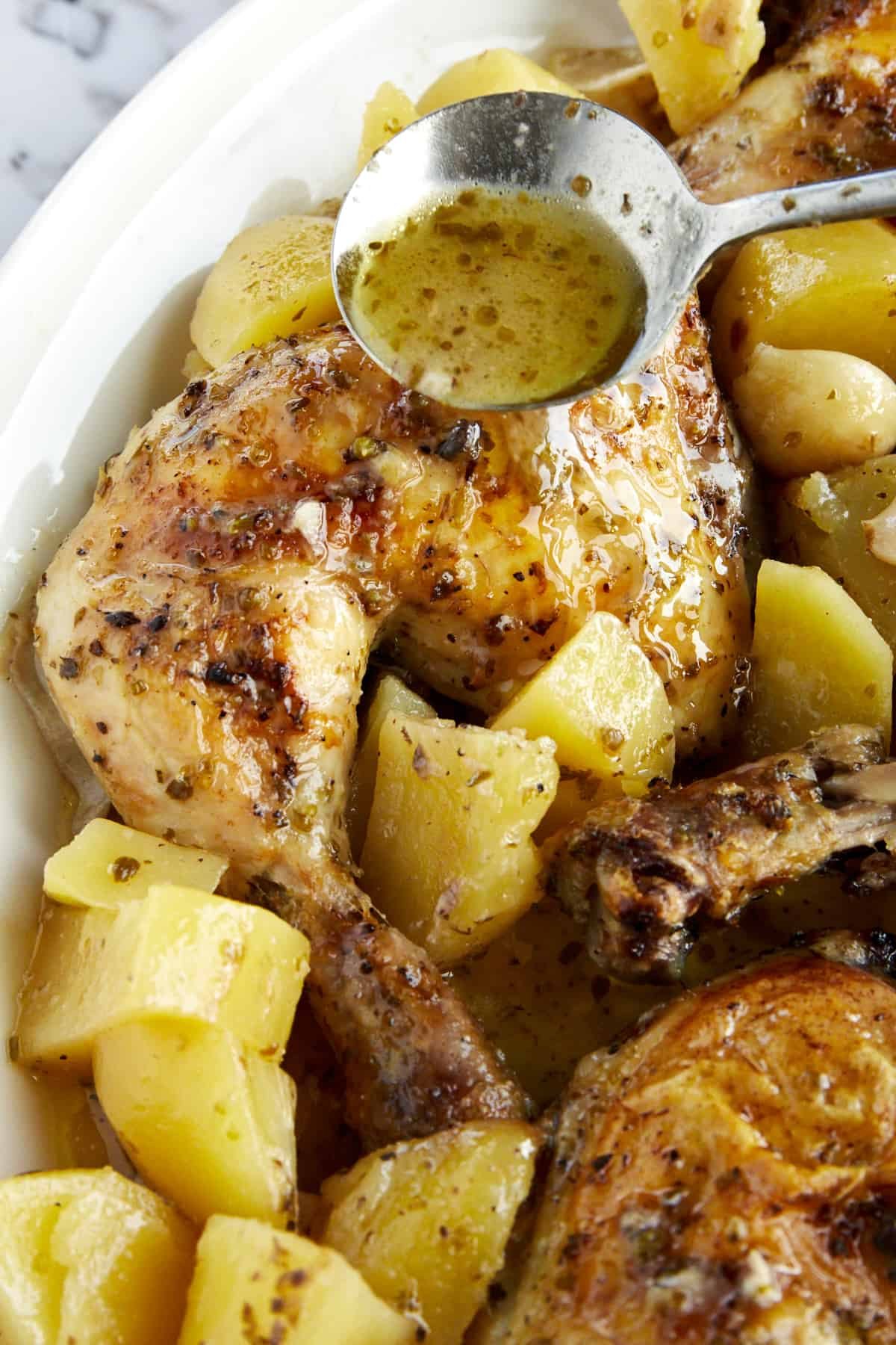 Olive oil seasoning being drizzled over cooked Greek chicken and potatoes.