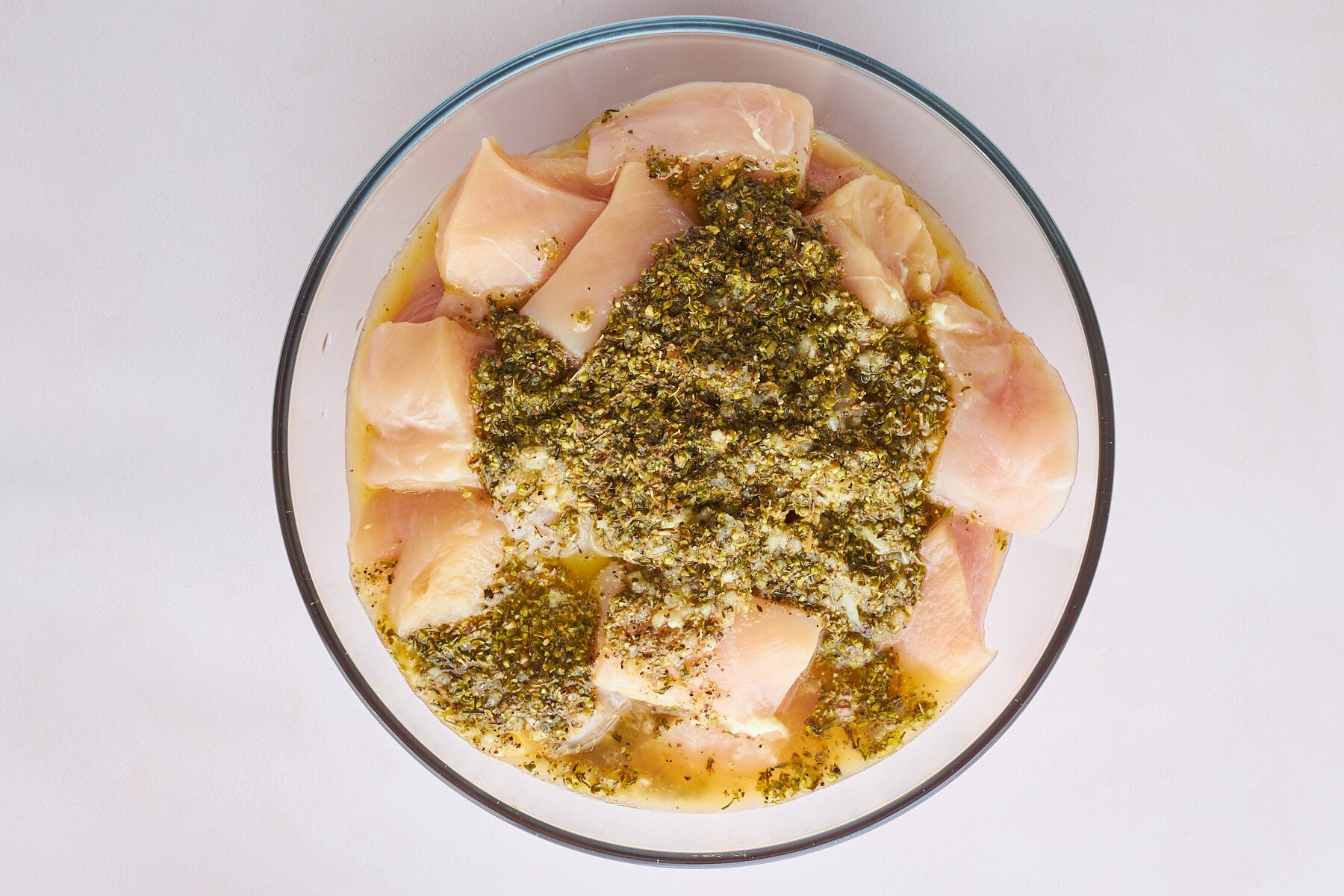 Raw chicken pieces marinading in a bowl of souvlaki marinade.