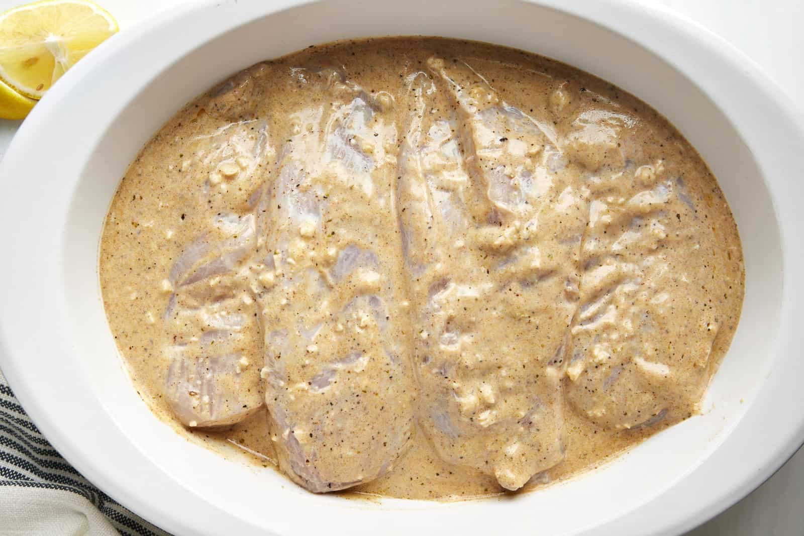 Chicken breasts being marinated in a Greek yogurt sauce.