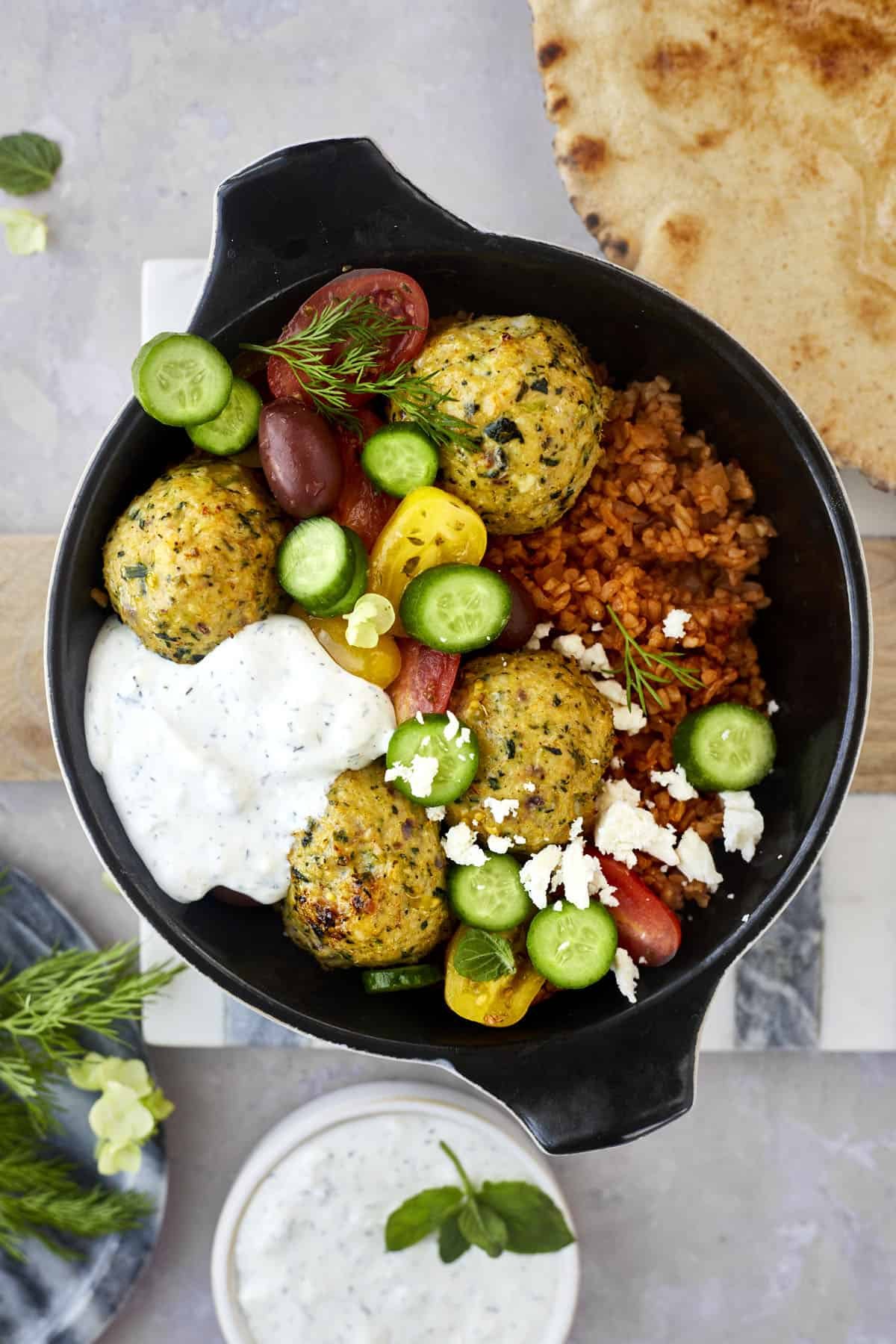 a skillet with rice, Greek meatballs, cucumber, tomatoes, and tzatziki