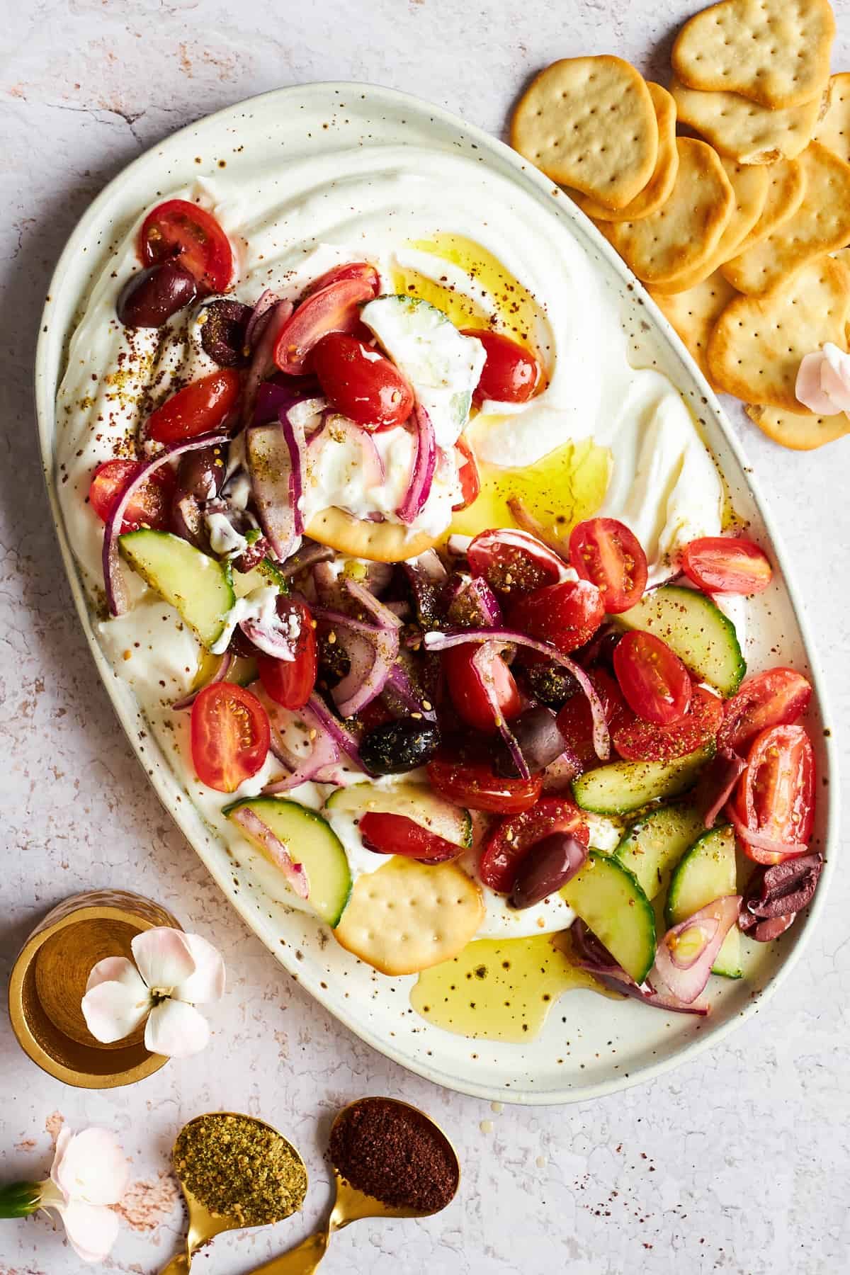 A platter of Greek salad dip with crackers on the side.