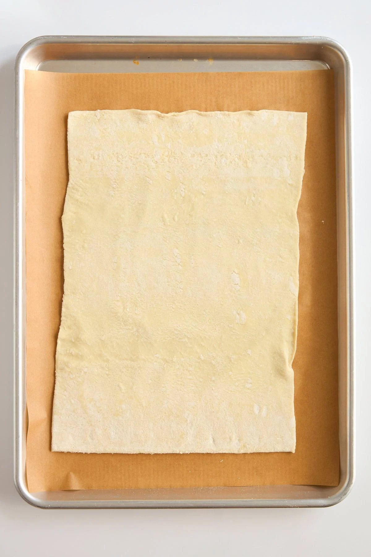 A sheet of uncooked puff pastry is placed on a piece of parchment paper on a baking tray, ready for baking.