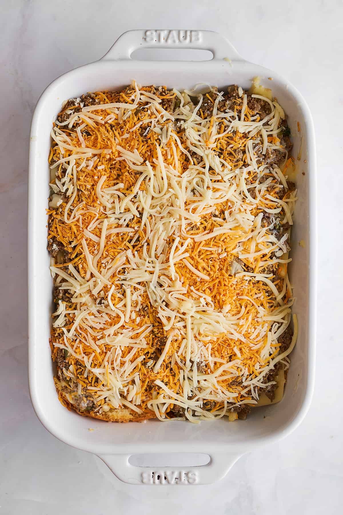 Ground beef sliders being layered in a baking dish.