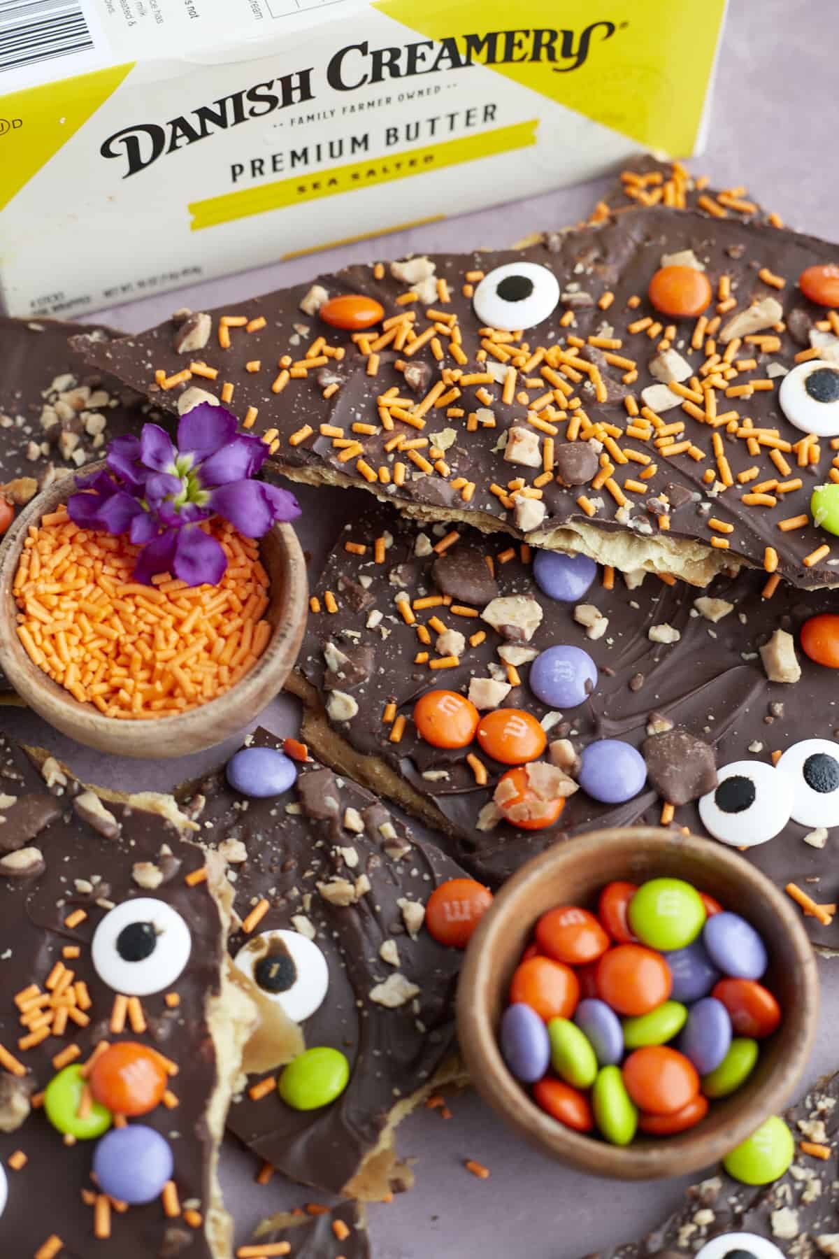 pieces of Halloween saltine crack candy with small bowls of m&ms and orange sprinkles in between
