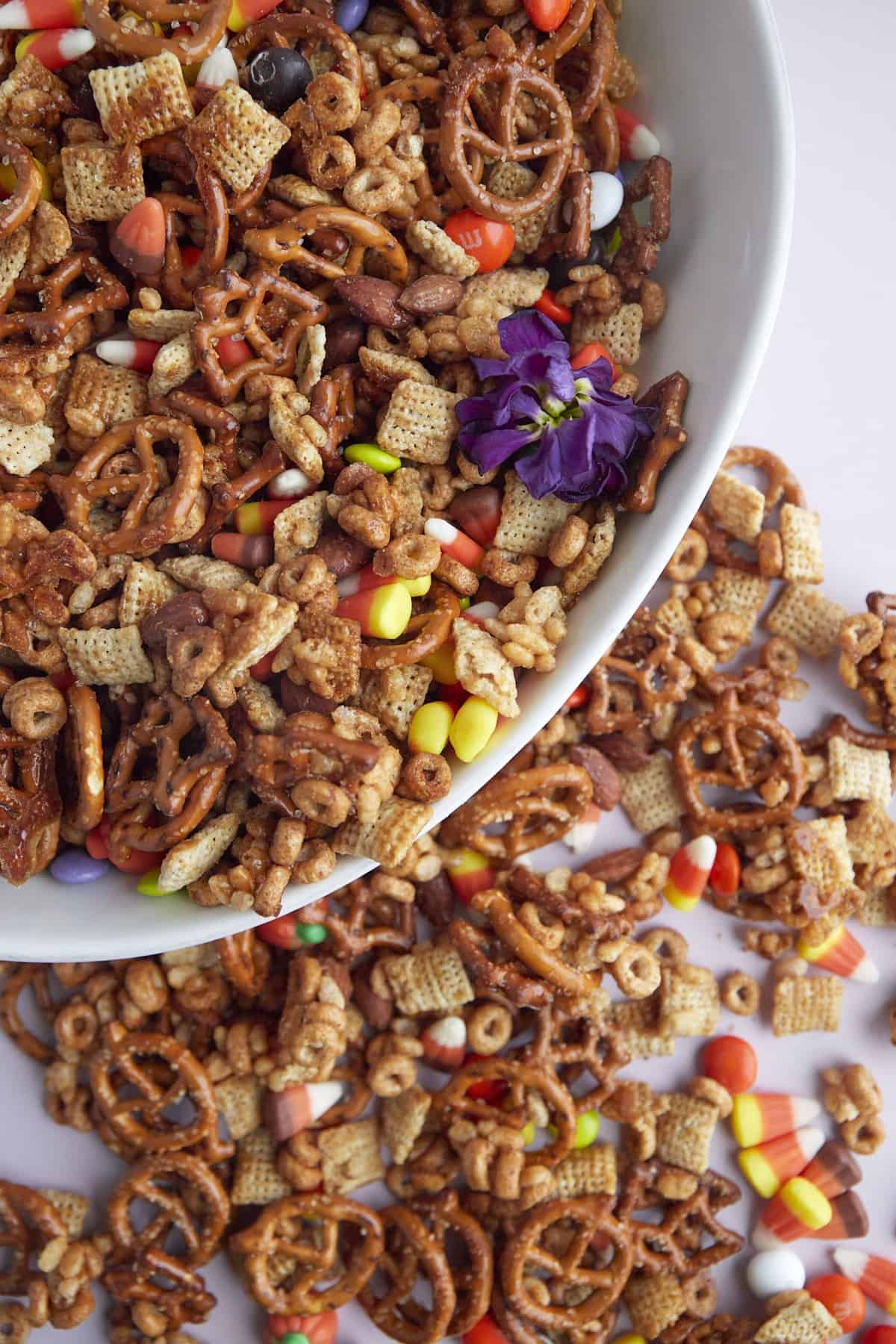 a white bowl full of Halloween snack mix with more mix scattered on a table around it