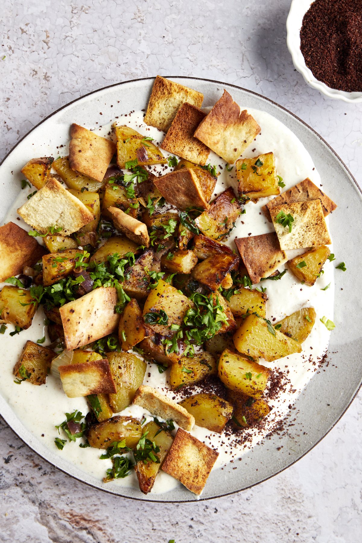 A bowl of whipped tahini topped with harissa potatoes and air fried pita.