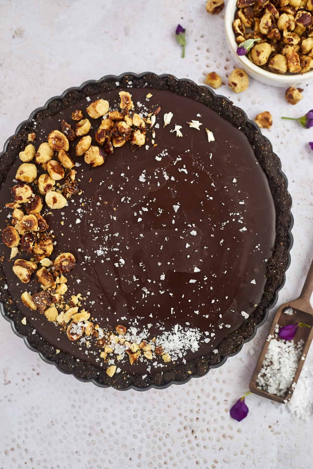 overhead image of a hazelnut chocolate tart topped with hazelnuts and sea salt