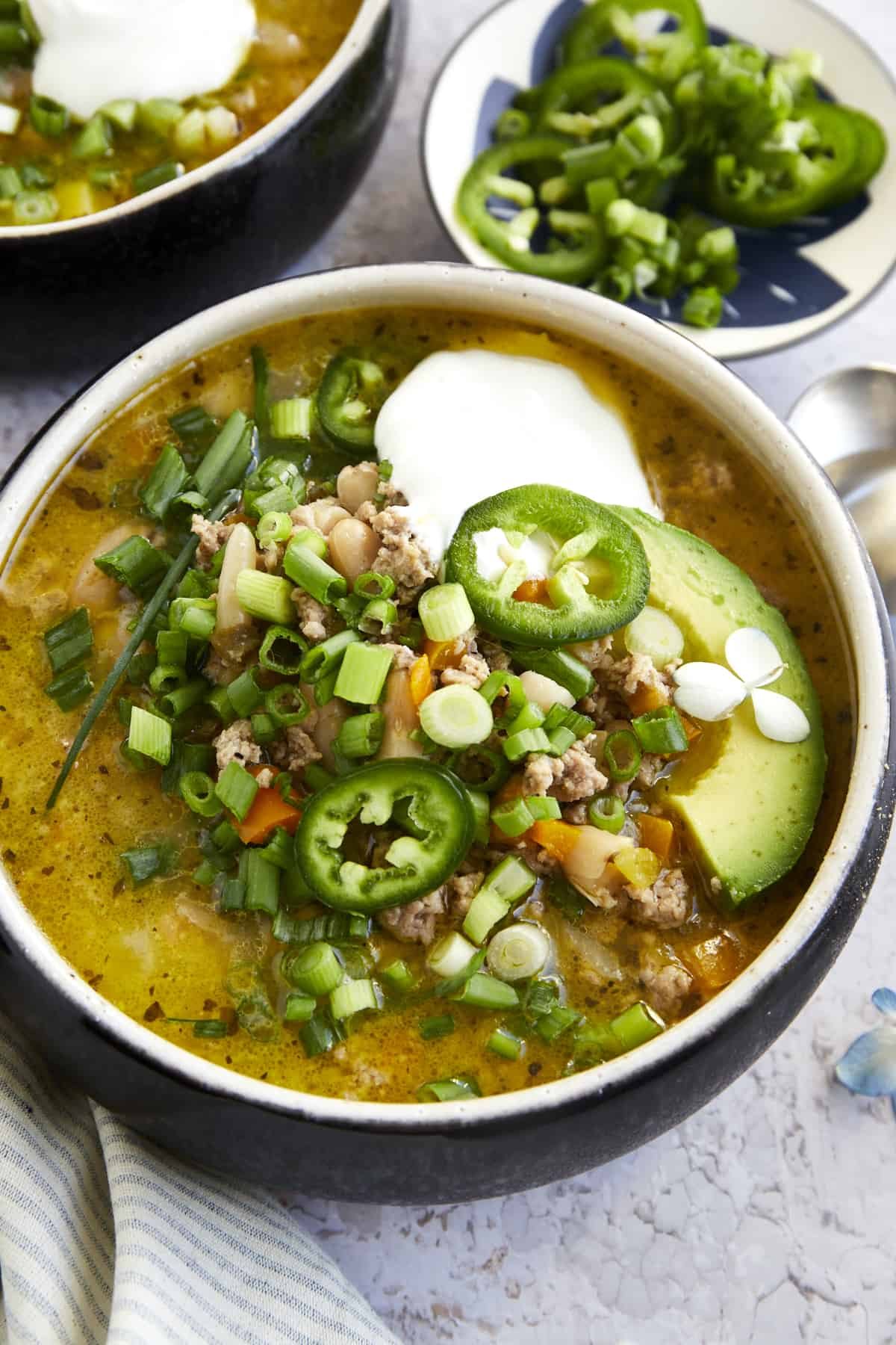 A bowl of healthy white turkey chili with scallions, jalapeño, avocado, and sour cream.