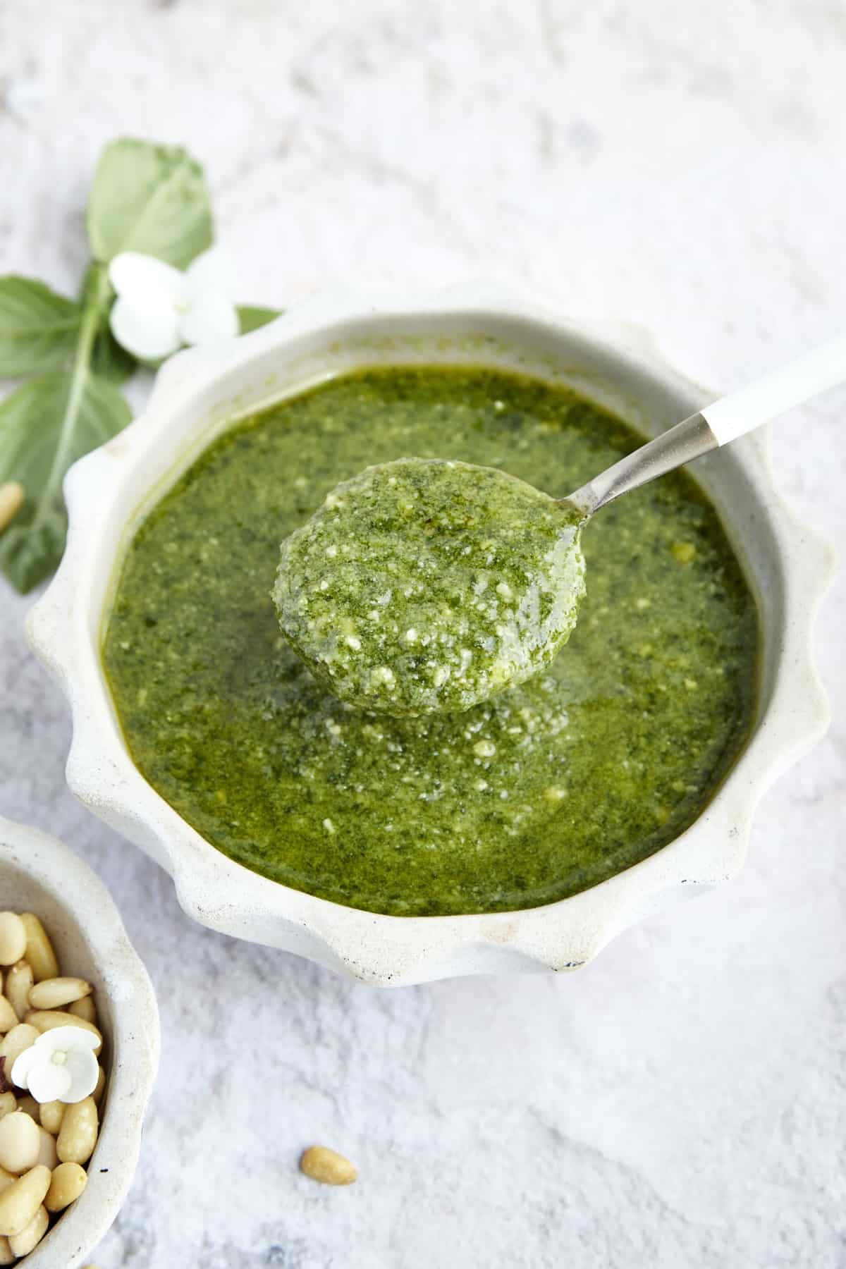 A spoon scooping up a spoonful of homemade basil pesto from a bowl.