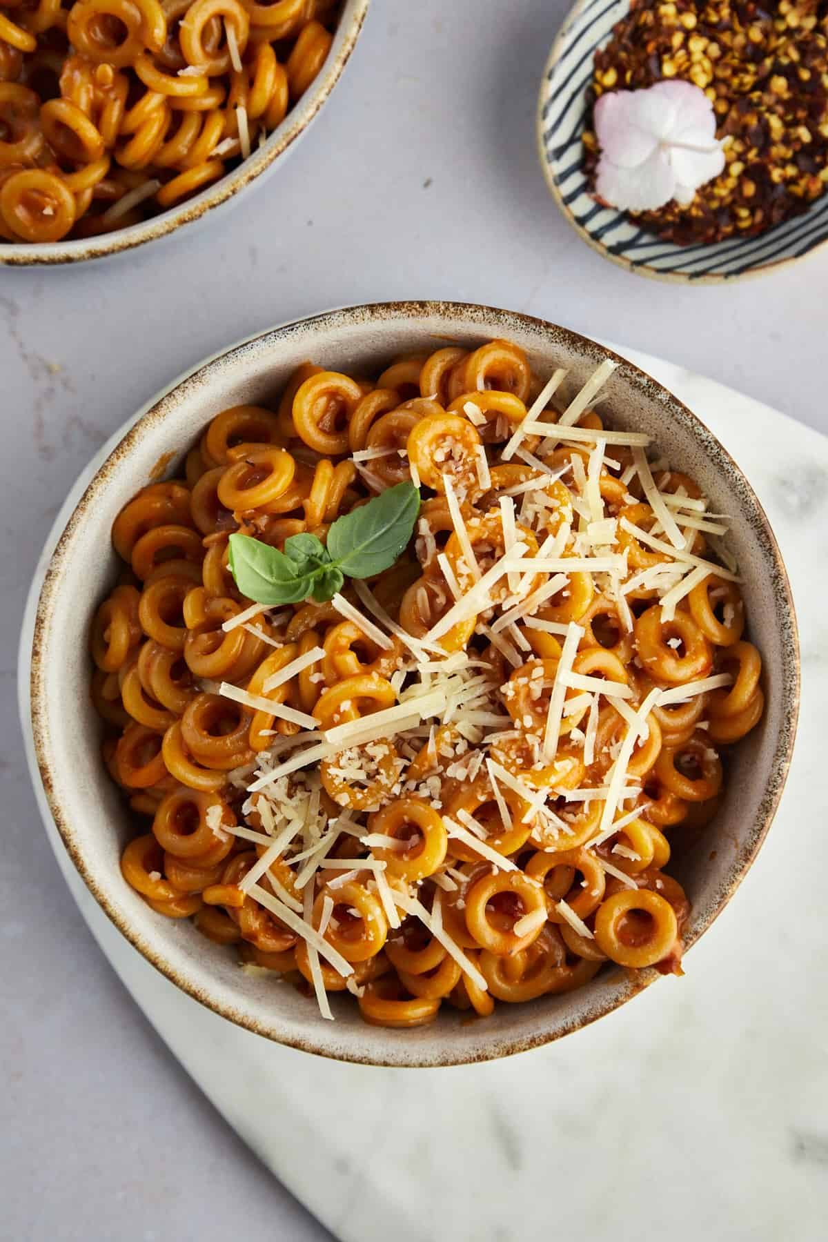 overhead image of a bowl of spaghetti o's topped with Parmesan chese and basil