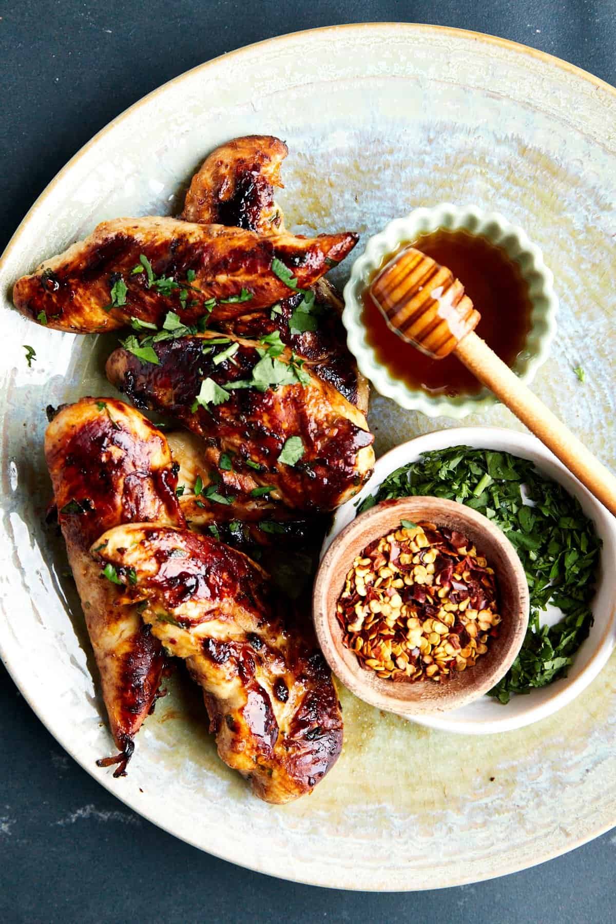 A bowl of honey garlic chicken tenders with honey, chili flakes, and green onions.