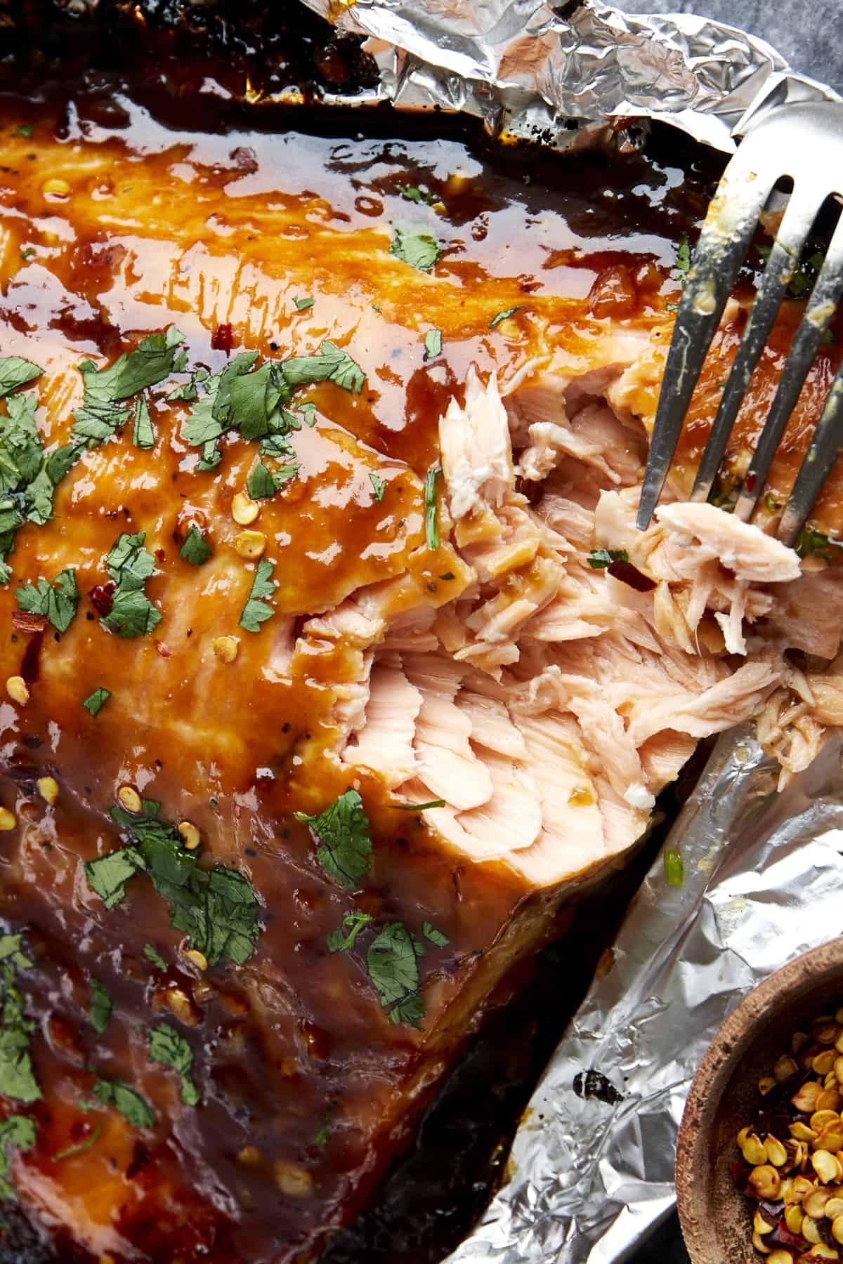 A fork tearing a bite of honey garlic salmon from a large filet.