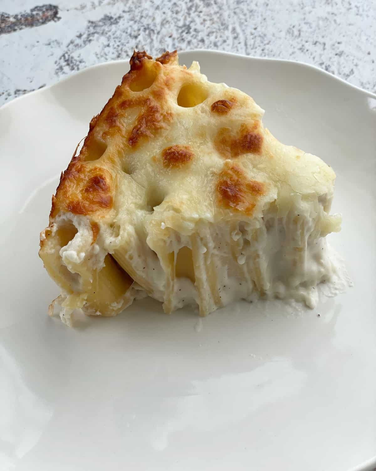 A triangular slice of rigatoni pie on a white plate.