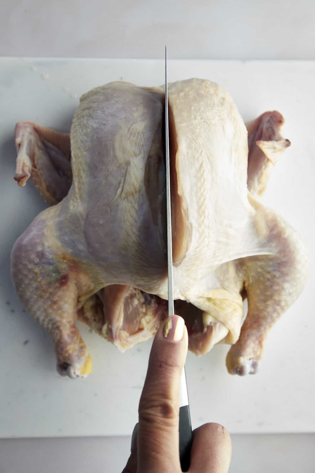 A knife slicing down the backbone of the chicken.