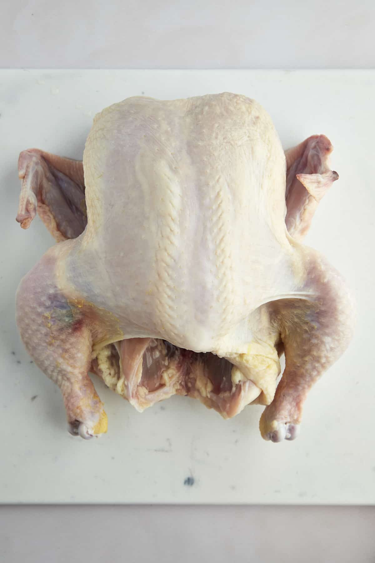 A raw whole chicken on a cutting board.