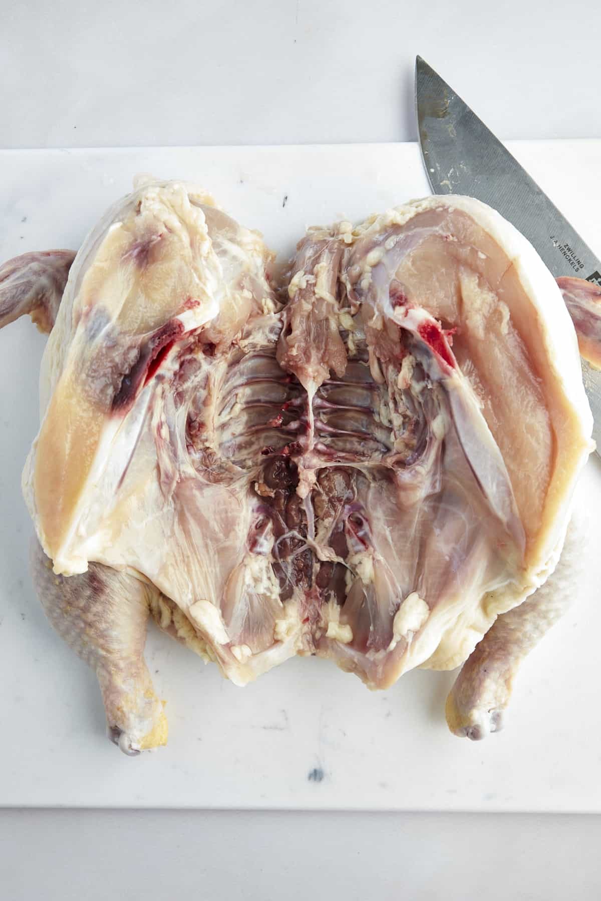 An open, raw butterflied chicken.