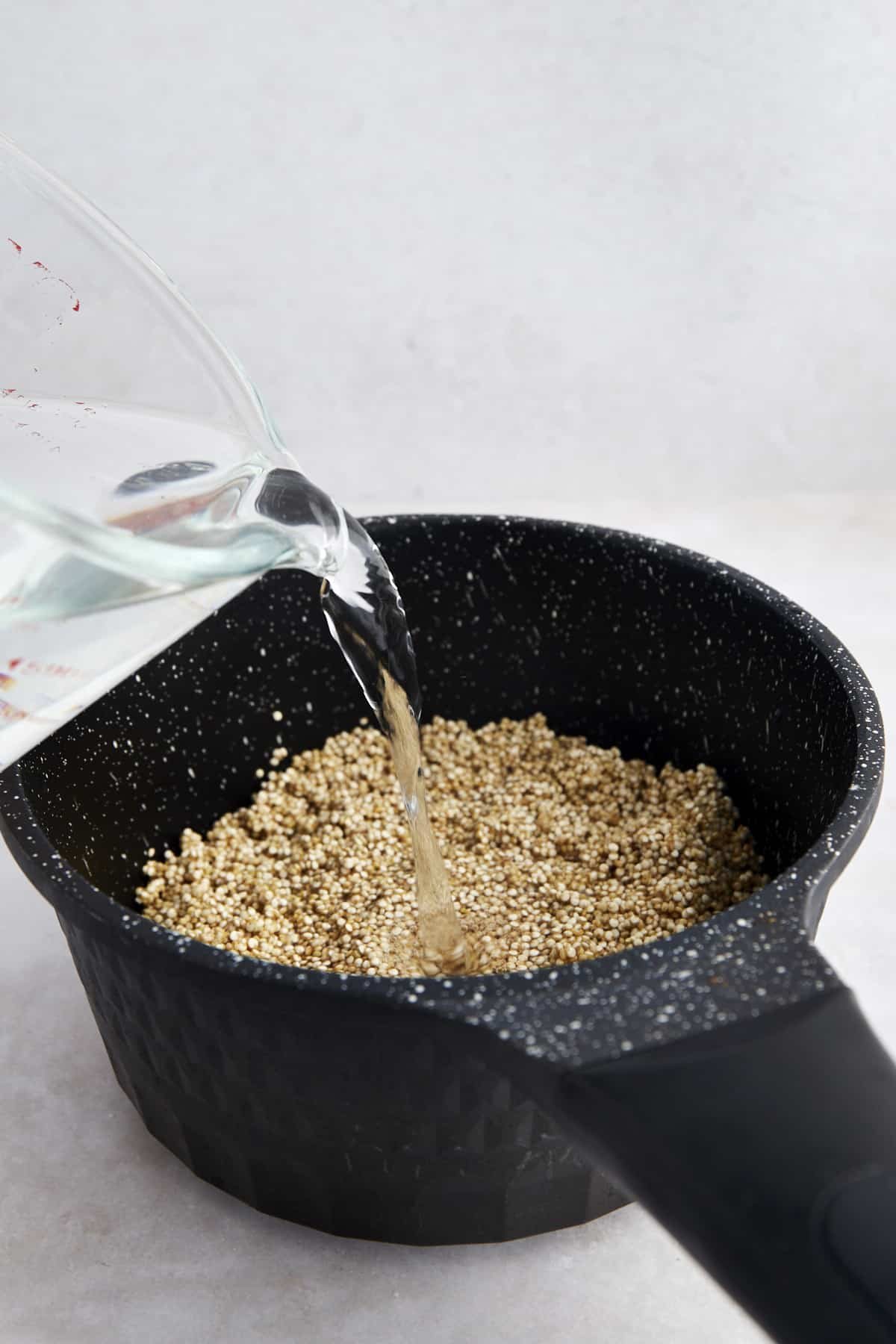 Water being poured into a pot full of uncooked white quinoa.