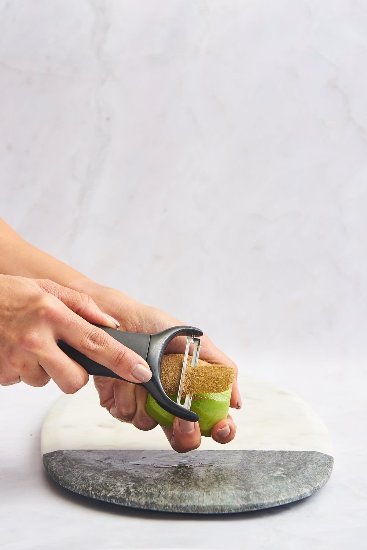 A vegetable peeler being used to peel the skin off a kiwi.