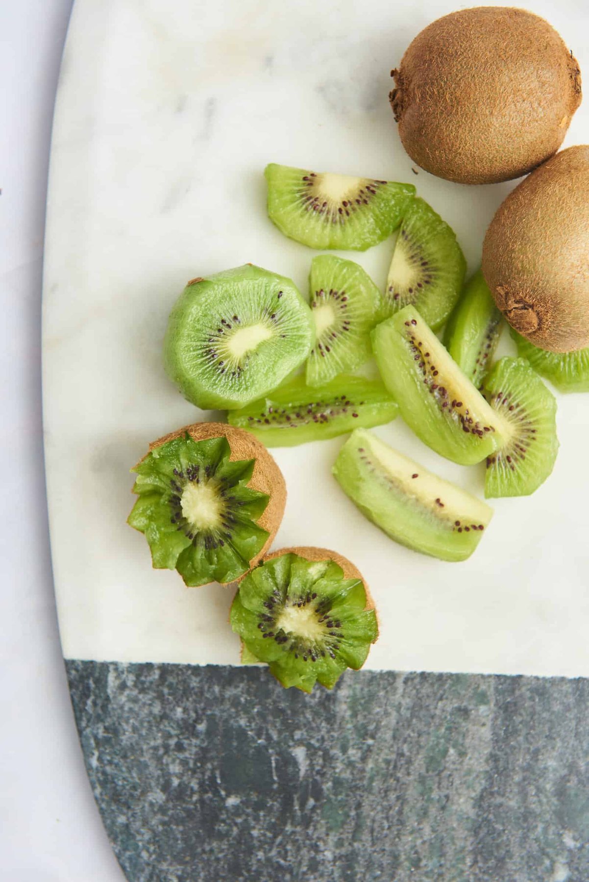 Whole kiwis, kiwi wedges, and star shaped kiwi on a cutting board.