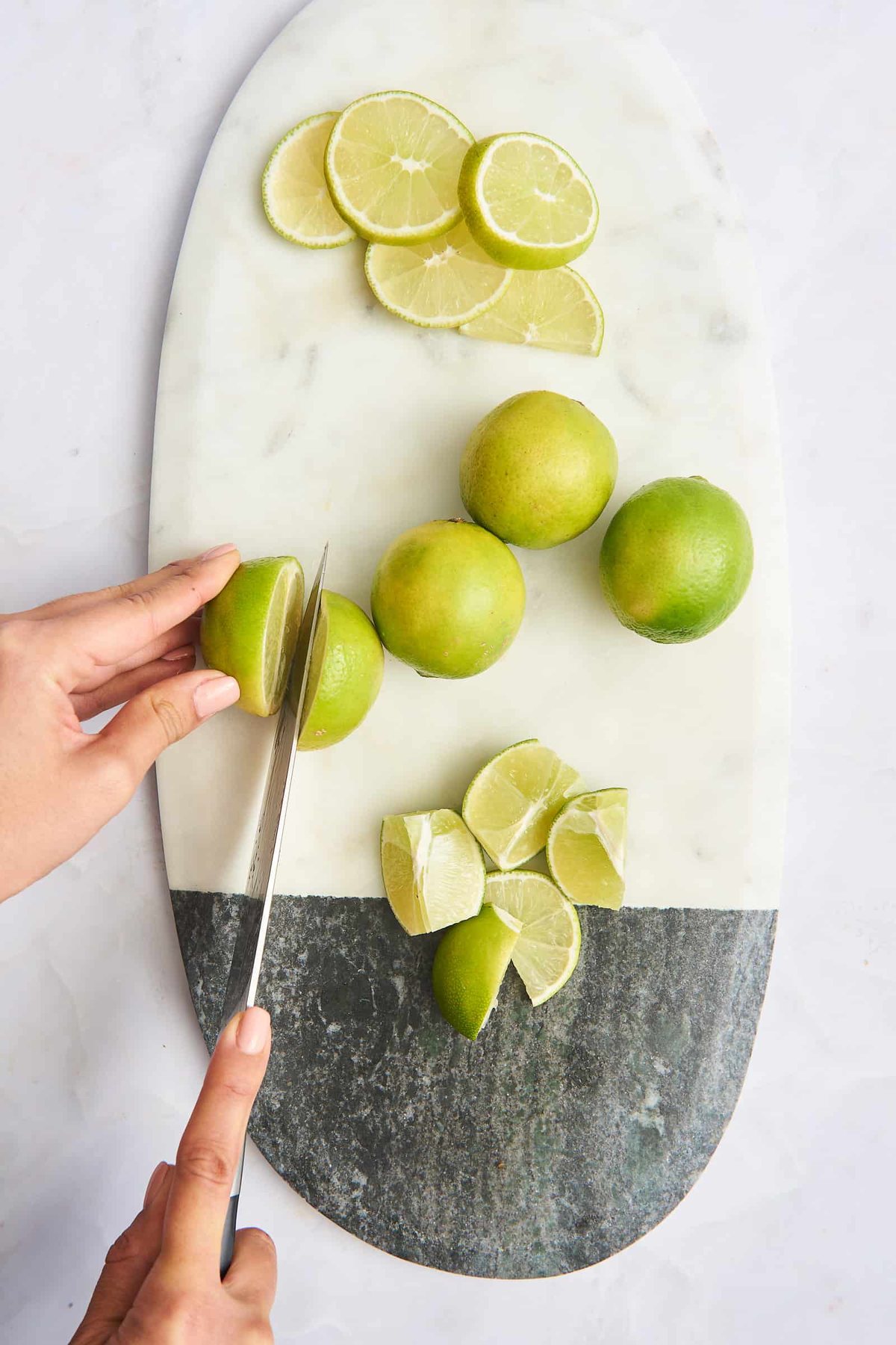 Lime rounds, whole limes, lime wedges, and a lime being halved on a cutting board.