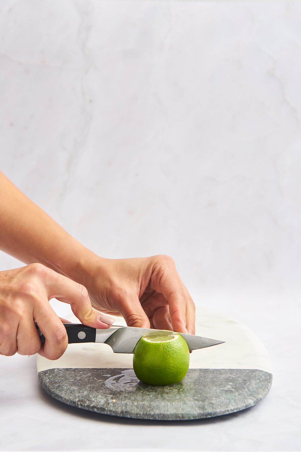 A lime being sliced in half on a marble cutting board.