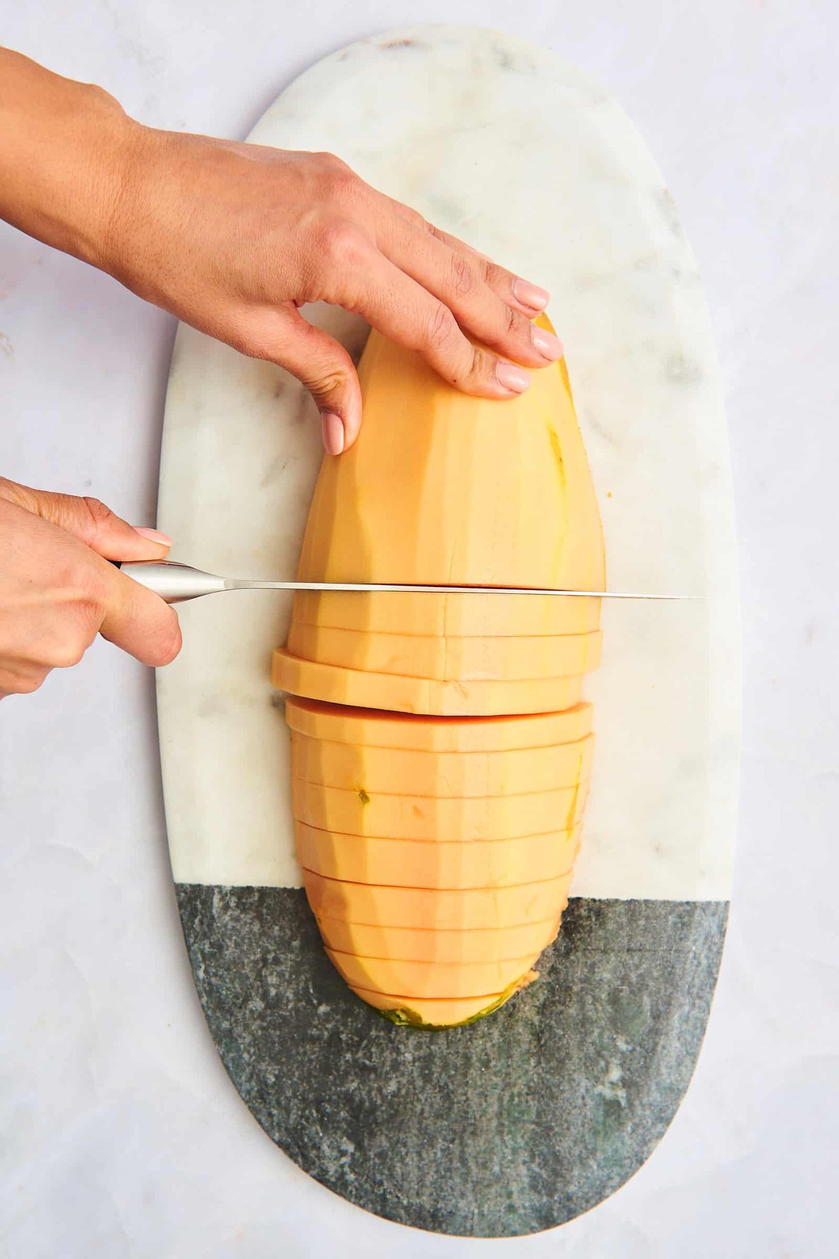 A hand slicing a papaya into half rings.