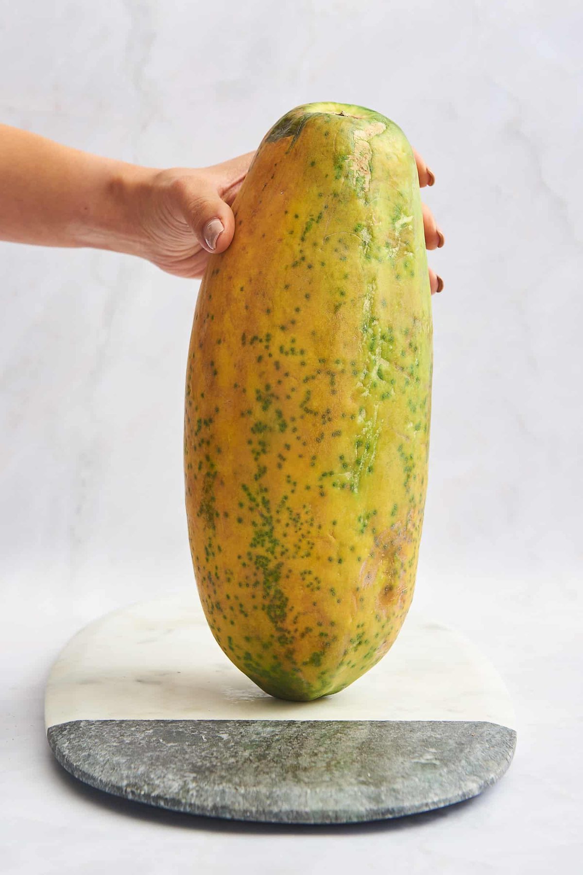 A hand holding a whole papaya.