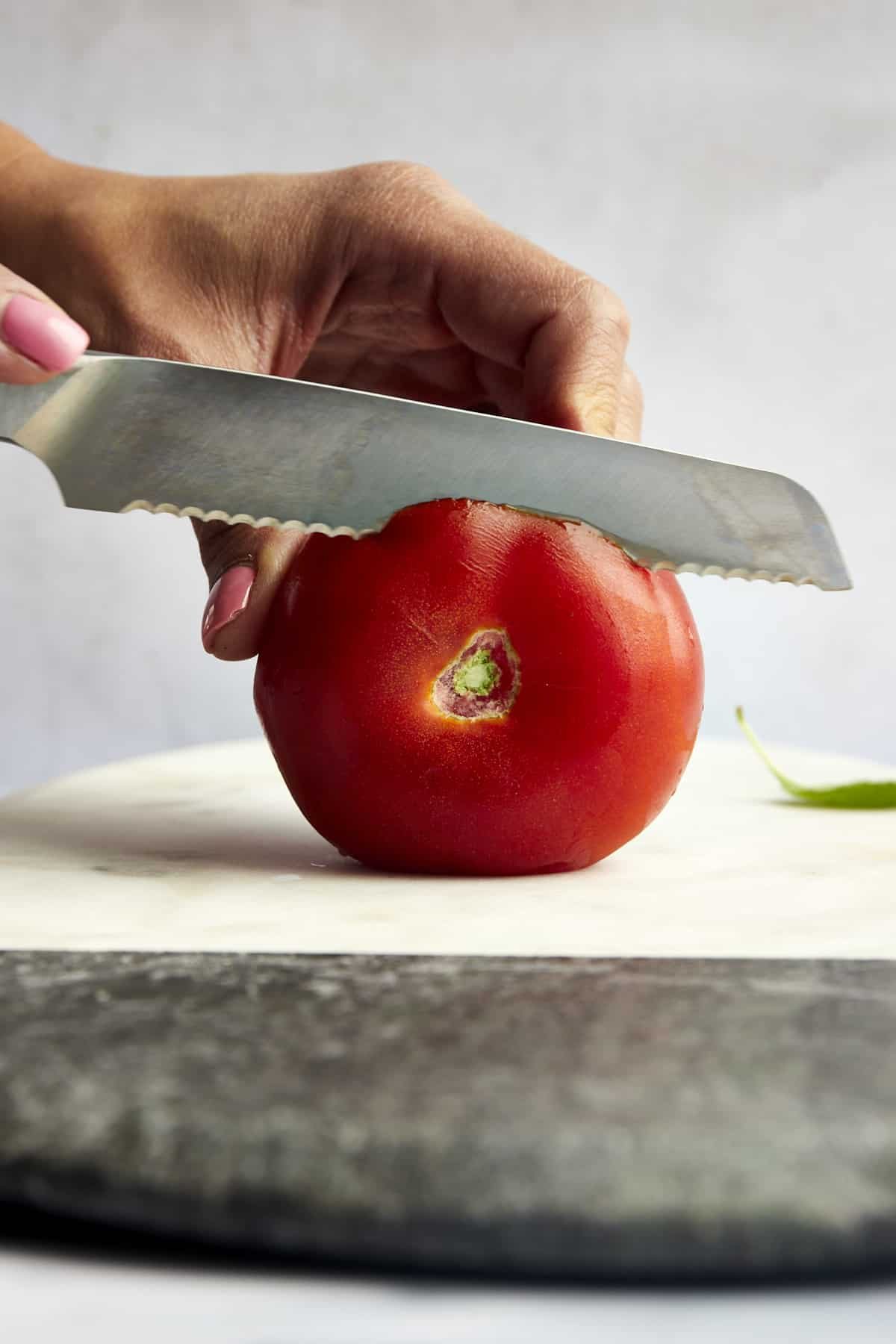 Side view of the top of a tomato being sliced off.